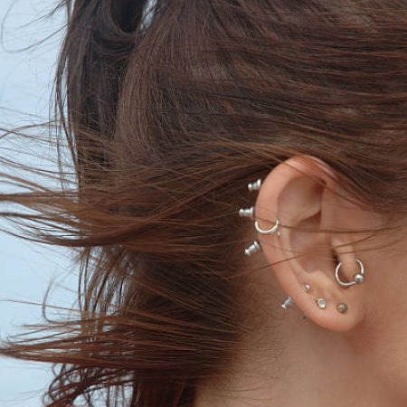 Close-up of multiple ear piercings on young woman with wind-swept hair. Slightly soft focus.